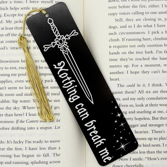 A black Nothing Can Break Me Sword Metal Bookmark on an open book with a gold tassel