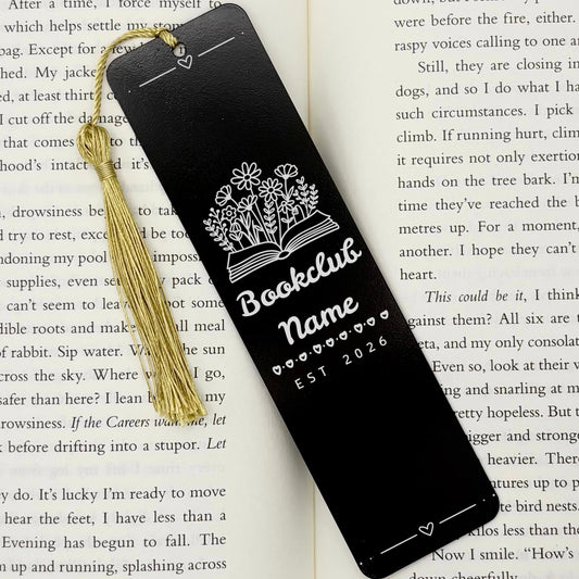 A black Personalised Book Club Name Metal Bookmark on an open book with a gold tassel