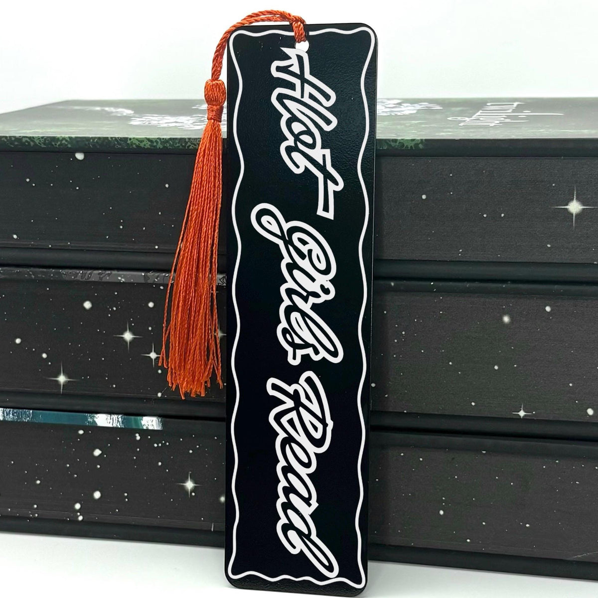 Hot Girls Read Metal Engraved Bookmark with a red tassel on a patterned background.
