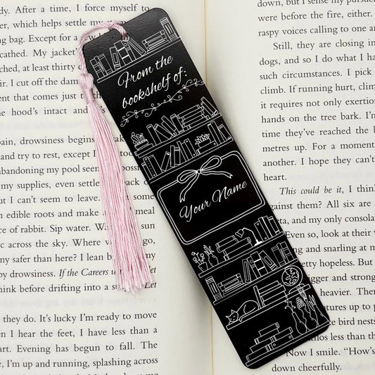A black Personalised Name Bookshelf Metal Bookmark on an open book with a pink tassel