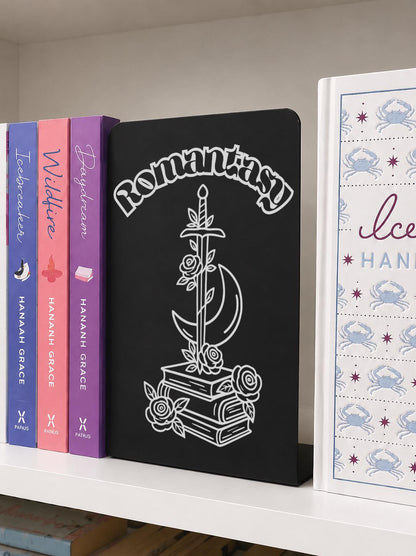     Romantasy Genre Metal Bookshelf Sign Bookend displayed on a bookshelf beside colourful romance and fantasy novels.