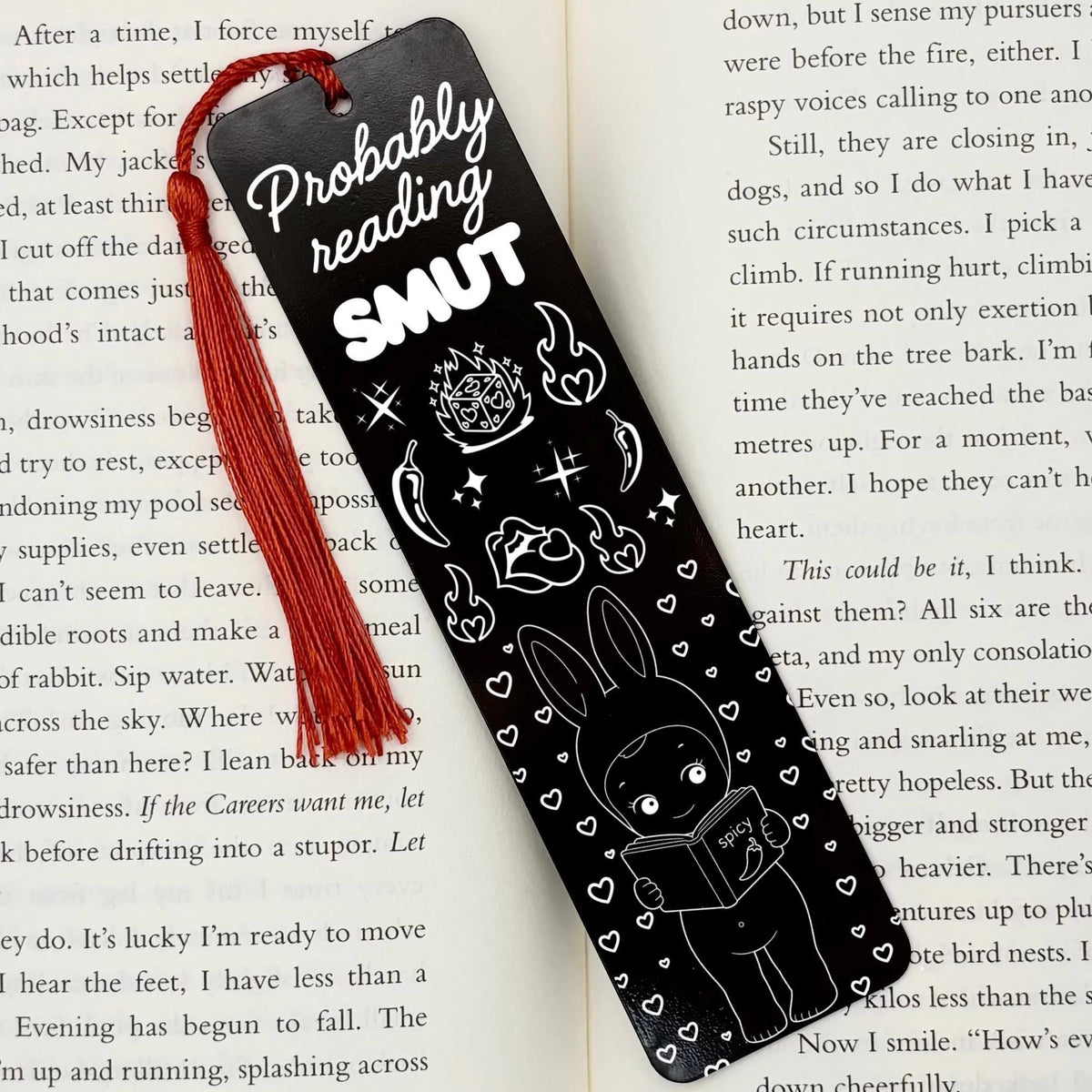 A black Probably Reading Smut Metal Bookmark on an open book with red tassel
