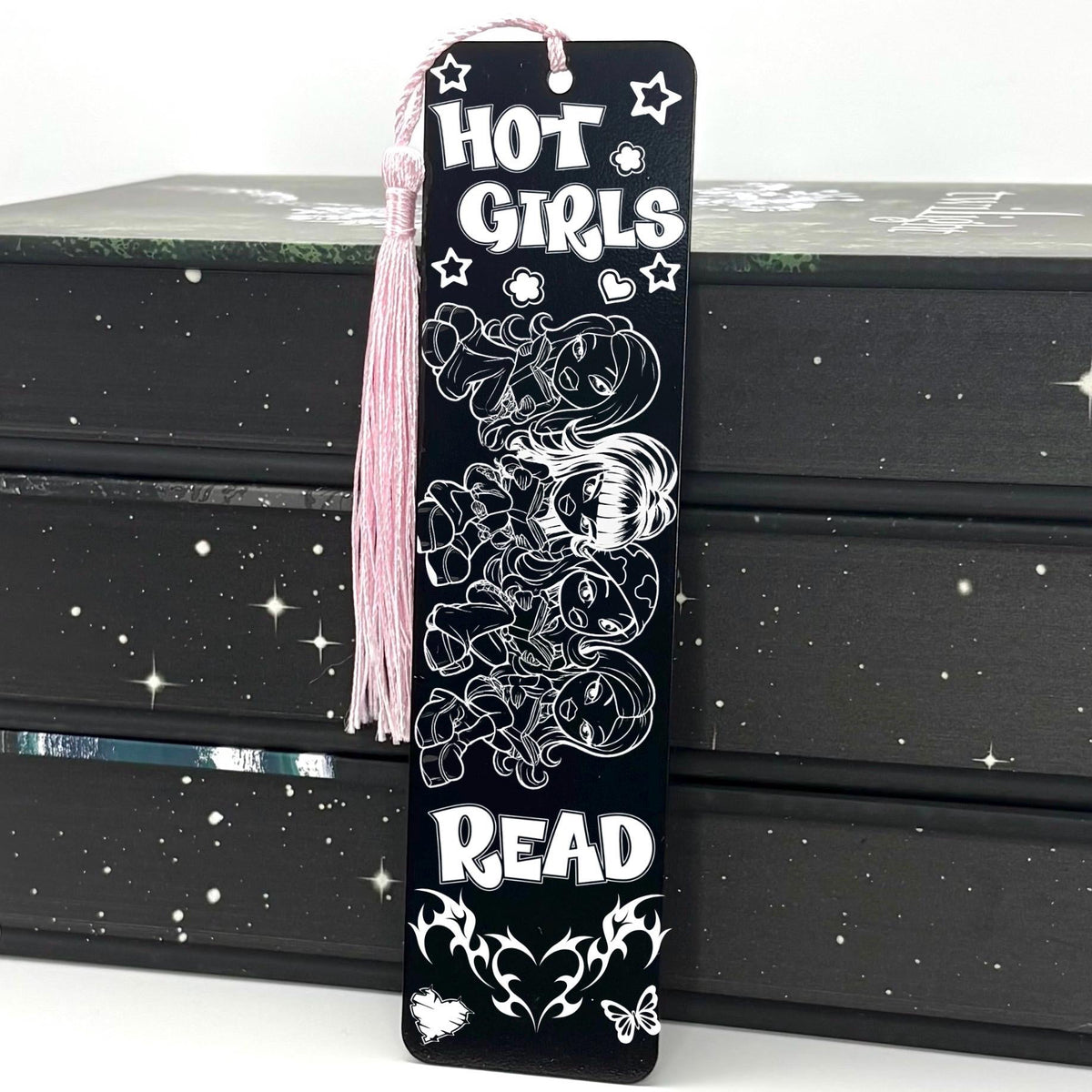 A black Y2K Hot Girls Read Metal Bookmark with pink tassel standing against a backdrop of books