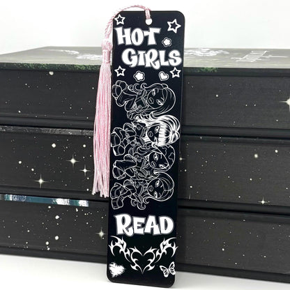 A black Y2K Hot Girls Read Metal Bookmark with pink tassel standing against a backdrop of books