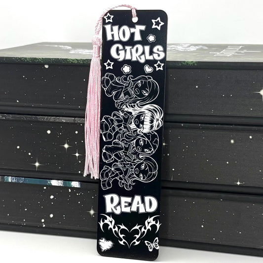A black Y2K Hot Girls Read Metal Bookmark with pink tassel standing against a backdrop of books