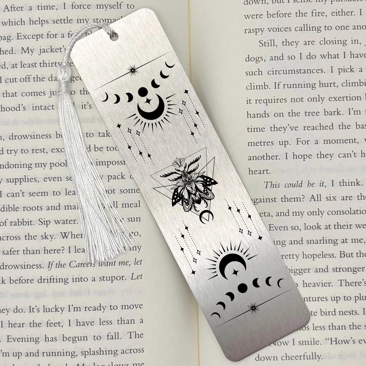 A brushed silver Celestial Moon and Stars Metal Bookmark on and open book with a white tassel