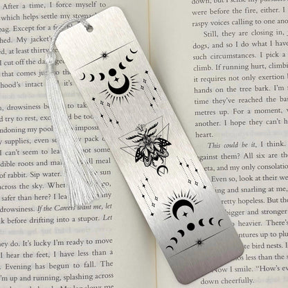A brushed silver Celestial Moon and Stars Metal Bookmark on and open book with a white tassel