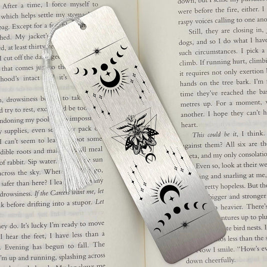 A brushed silver Celestial Moon and Stars Metal Bookmark on and open book with a white tassel