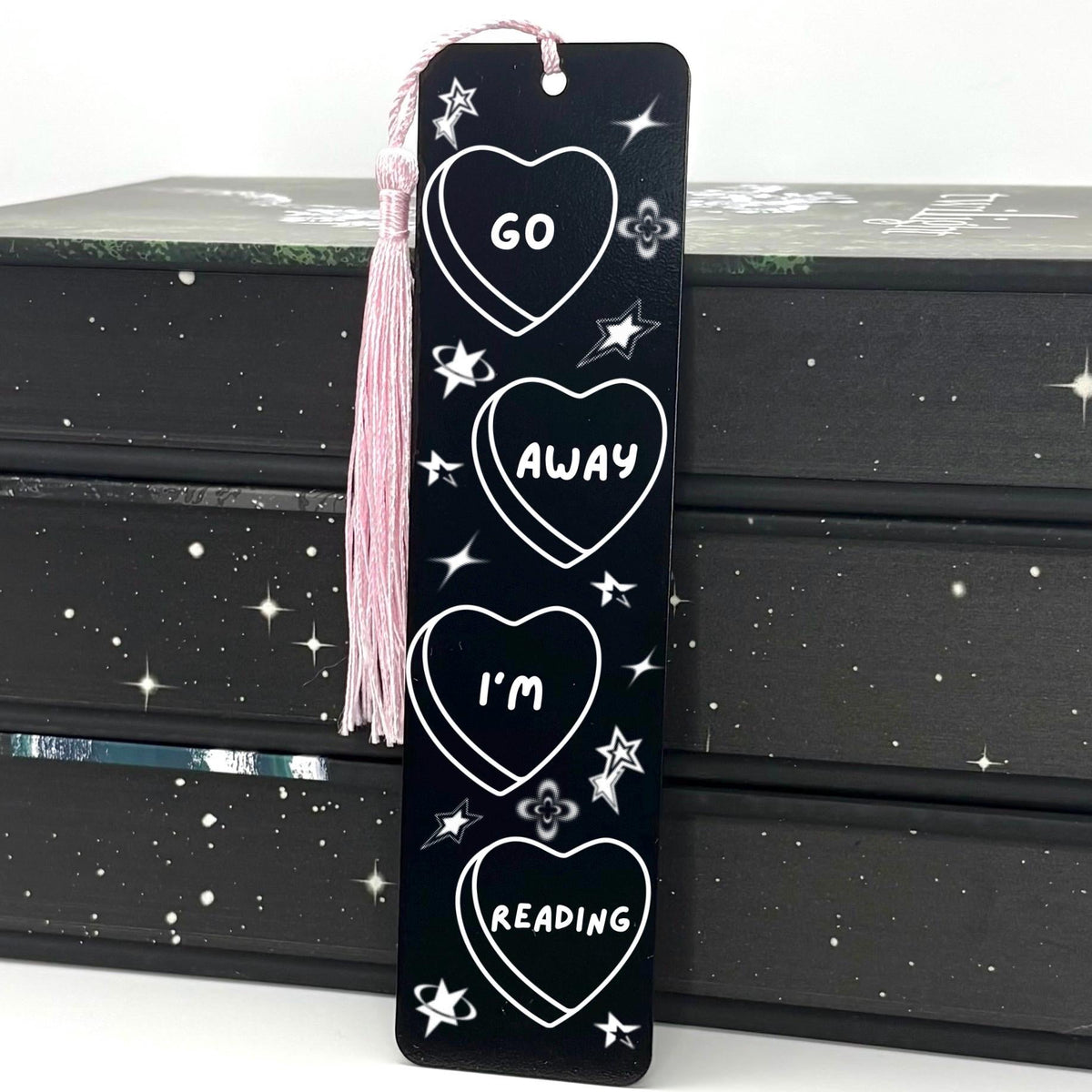     Go Away I’m Reading Metal Bookmark in black with heart, star and celestial design and pink tassel