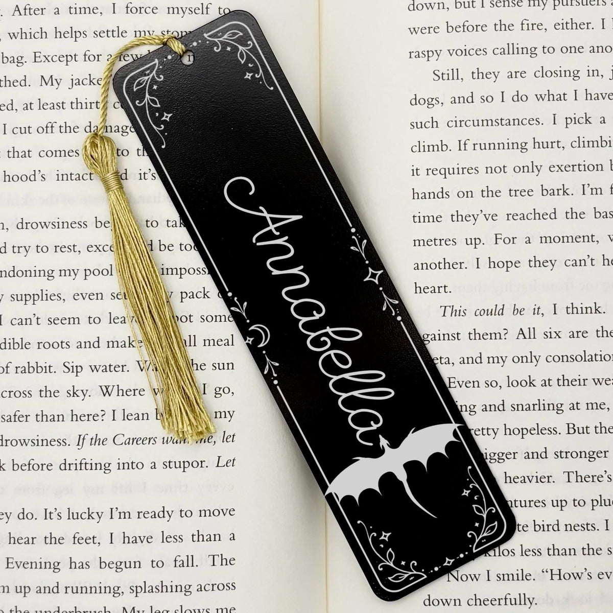     Personalised Name Dragon Bookmark in black metal with custom name, dragon artwork and gold tassel displayed on an open book.