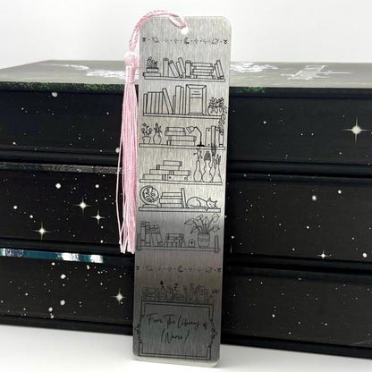 A brushed silver Personalised Name Library Shelf Metal Bookmark with pink tassel standing against a backdrop of books