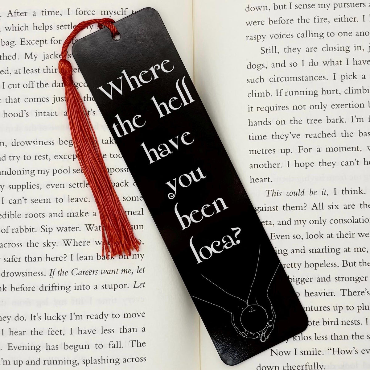     Where Have You Been Loca Metal Bookmark in black with red tassel, displayed on an open book.