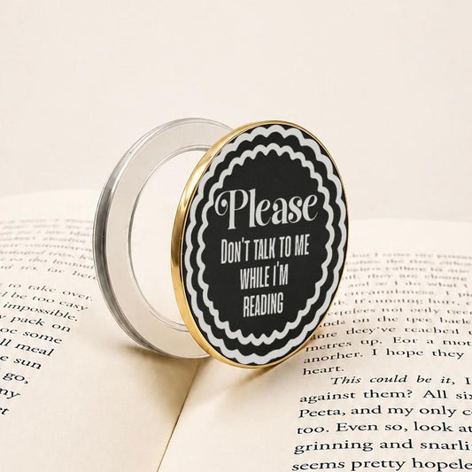    Don’t Talk To Me While I’m Reading Metal Kindle MagSafe Grip featuring a black and white engraved-style design with gold edging.