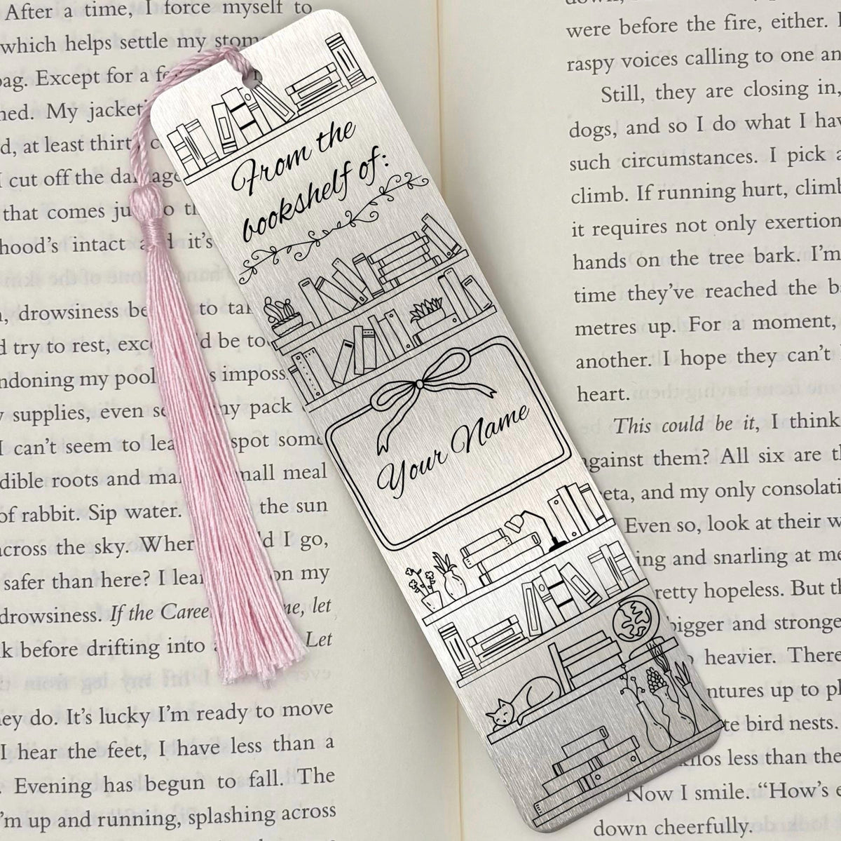 A brushed silver Personalised Name Bookshelf Metal Bookmark on an open book with a pink tassel