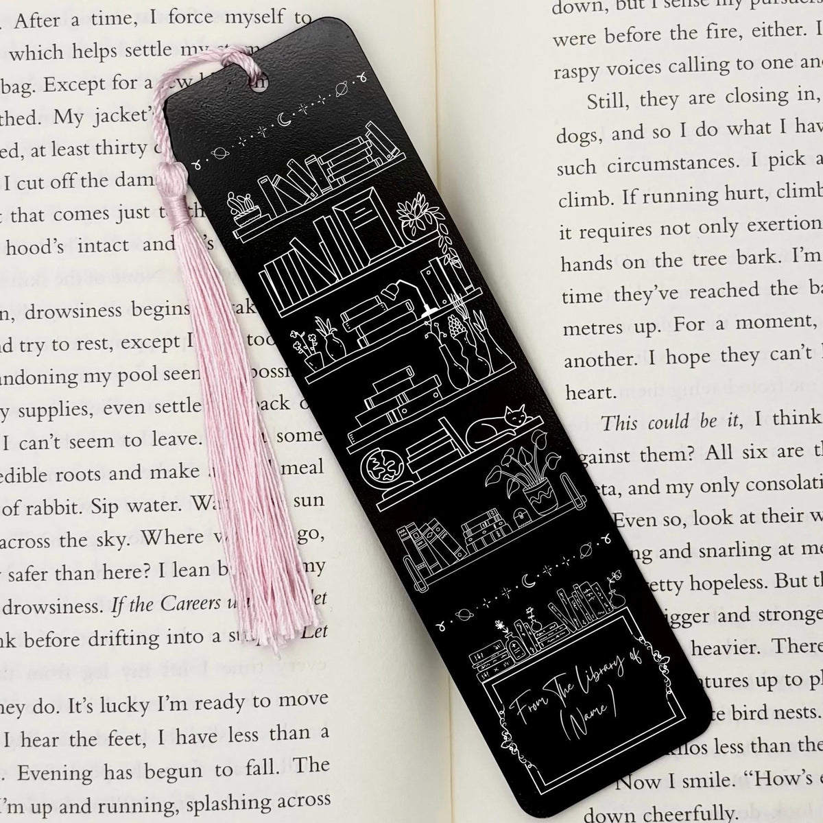 A black Personalised Name Library Shelf Metal Bookmark on and open book with a pink tassel
