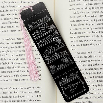 A black Personalised Name Library Shelf Metal Bookmark on and open book with a pink tassel