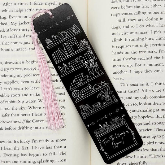 A black Personalised Name Library Shelf Metal Bookmark on and open book with a pink tassel