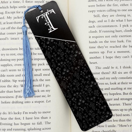 A black Personalised Floral Initial Metal Bookmark on an open book with light blue tassel