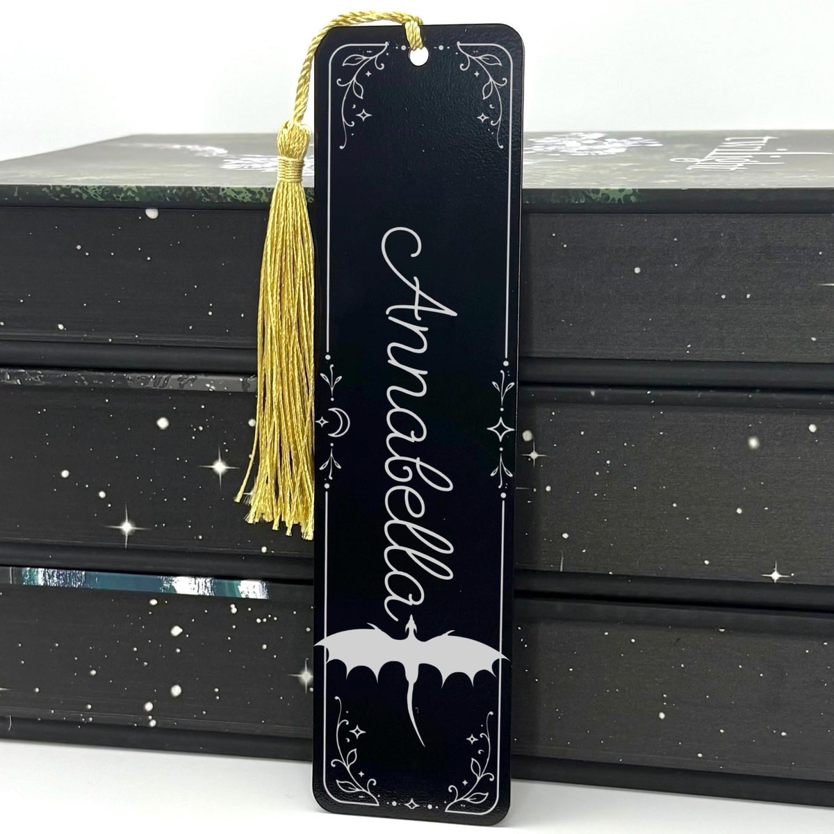     Personalised Name Dragon Bookmark in black metal featuring the name Annabella, engraved dragon design, celestial details and gold tassel.
