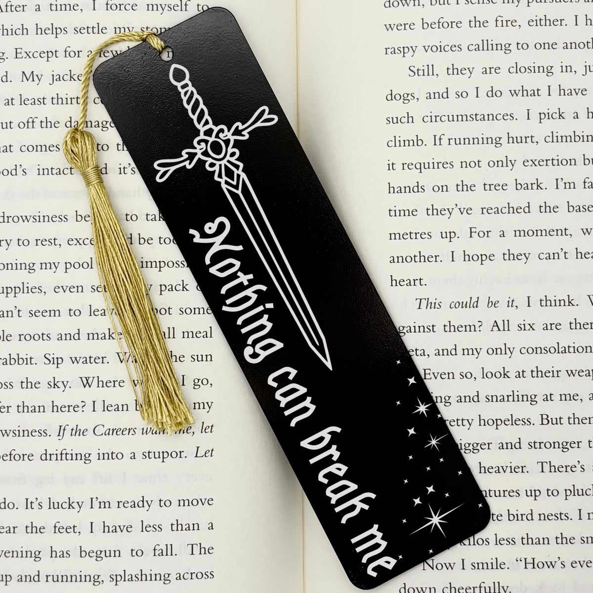 A black Nothing Can Break Me Sword Metal Bookmark on an open book with a gold tassel