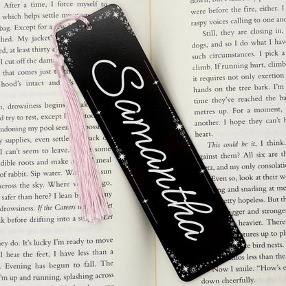 A black Personalised Name Metal Bookmark on an open book with a pink tassel