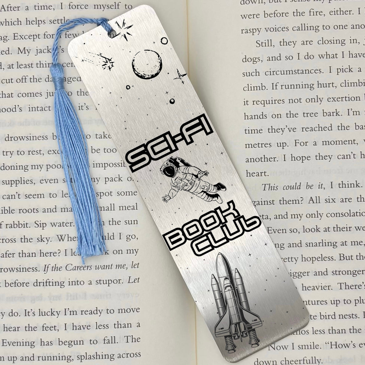     Sci-Fi Book Club Metal Bookmark in silver displayed on an open book with astronaut, stars and space shuttle design.