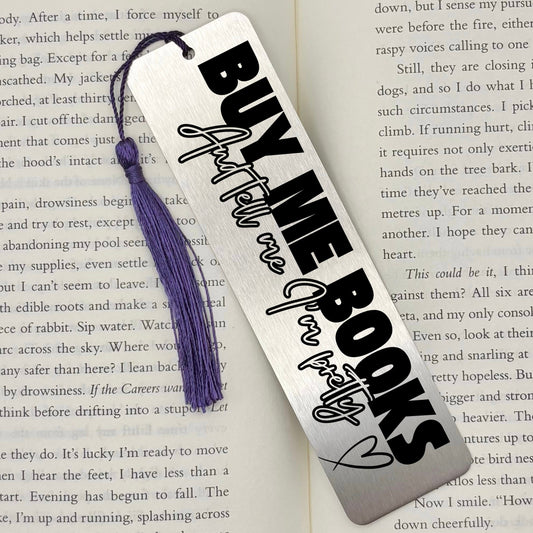A brushed silver Buy Me Books And Tell Me I’m Pretty Metal Bookmark Metal Bookmark with purple tassel on an open book