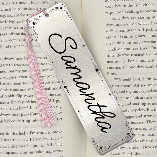 A brushed silver Personalised Name Metal Bookmark on an open book with a pink tassel