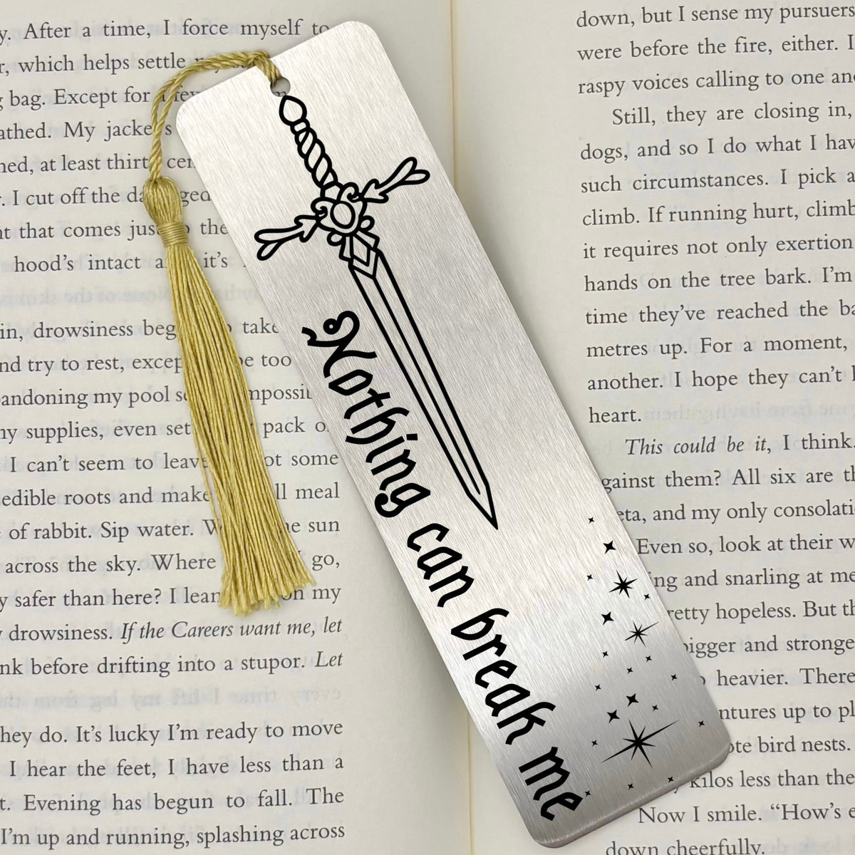 A brushed silver Nothing Can Break Me Sword Metal Bookmark on an open book with a gold tassel