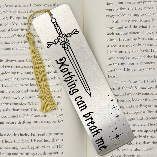 A brushed silver Nothing Can Break Me Sword Metal Bookmark on an open book with a gold tassel