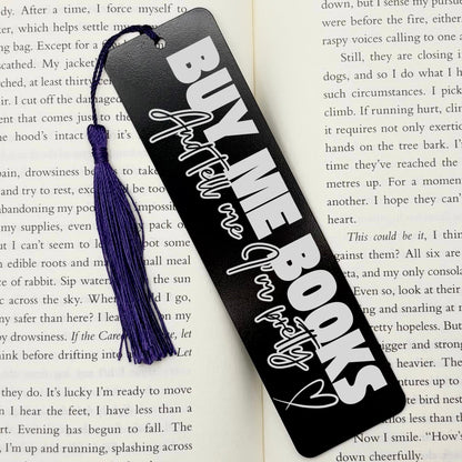 A black Buy Me Books And Tell Me I’m Pretty Metal Bookmark with purple tassel on an open book