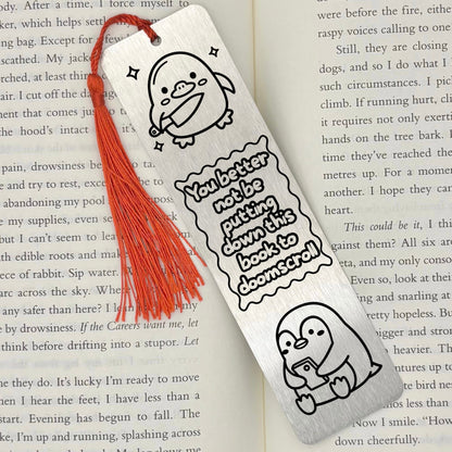 A brushed silver Doomscrolling Duck Metal Bookmark with red tassel on an open book