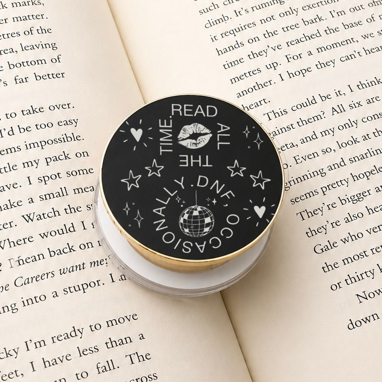     Read All The Time DNF Occasionally Metal MagSafe Kindle Grip displayed on an open book, showing the engraved reading-themed design.