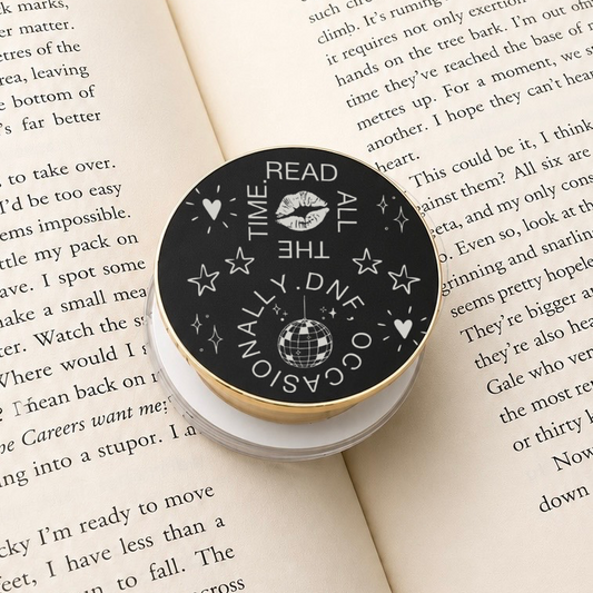     Read All The Time DNF Occasionally Metal MagSafe Kindle Grip displayed on an open book, showing the engraved reading-themed design.