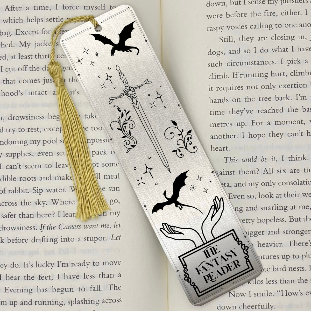 A brushed silver The Fantasy Reader Metal Bookmark on and open book with a gold tassel