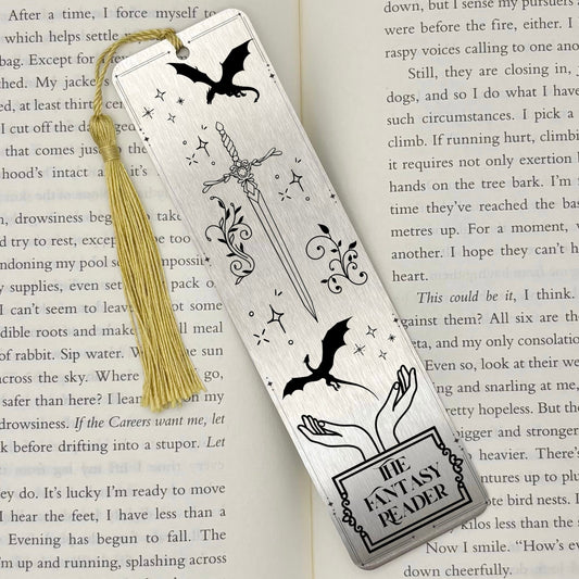 A brushed silver The Fantasy Reader Metal Bookmark on and open book with a gold tassel