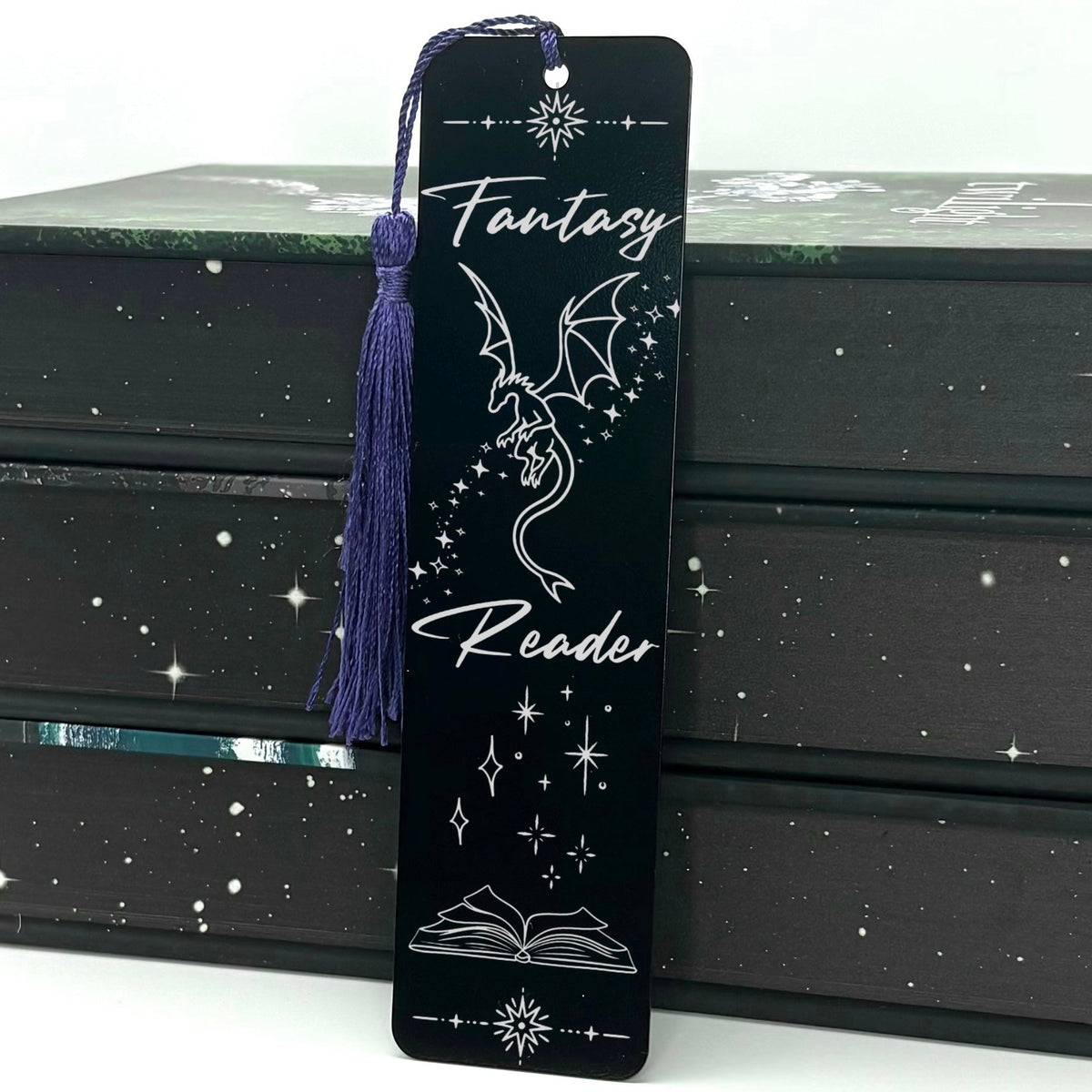A black Fantasy Reader Dragon Metal Bookmark with purple tassel standing against a backdrop of books