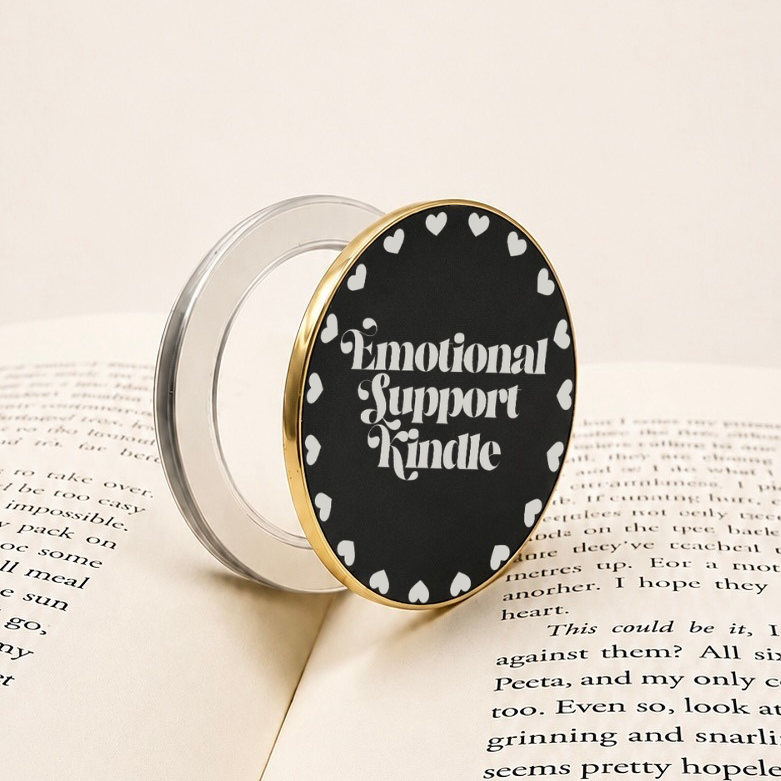 Emotional Support Kindle Metal E-Reader Grip resting on an open book with a heart design.
