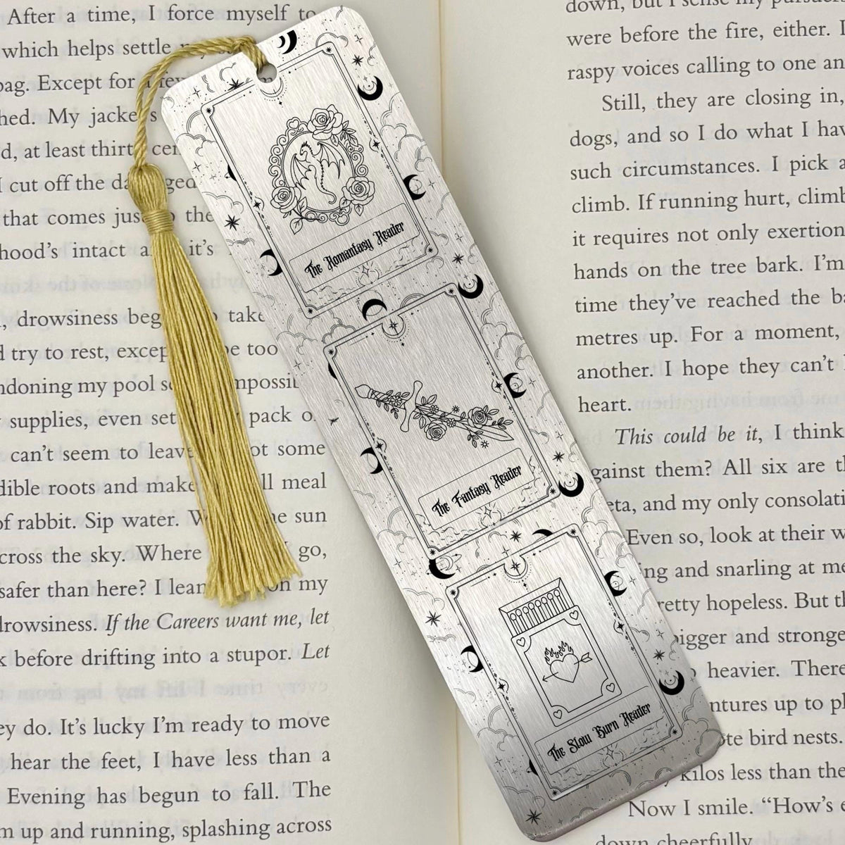 A brushed silver Fantasy Romantasy Slow Burn Metal Bookmark on an open book with a gold tassel