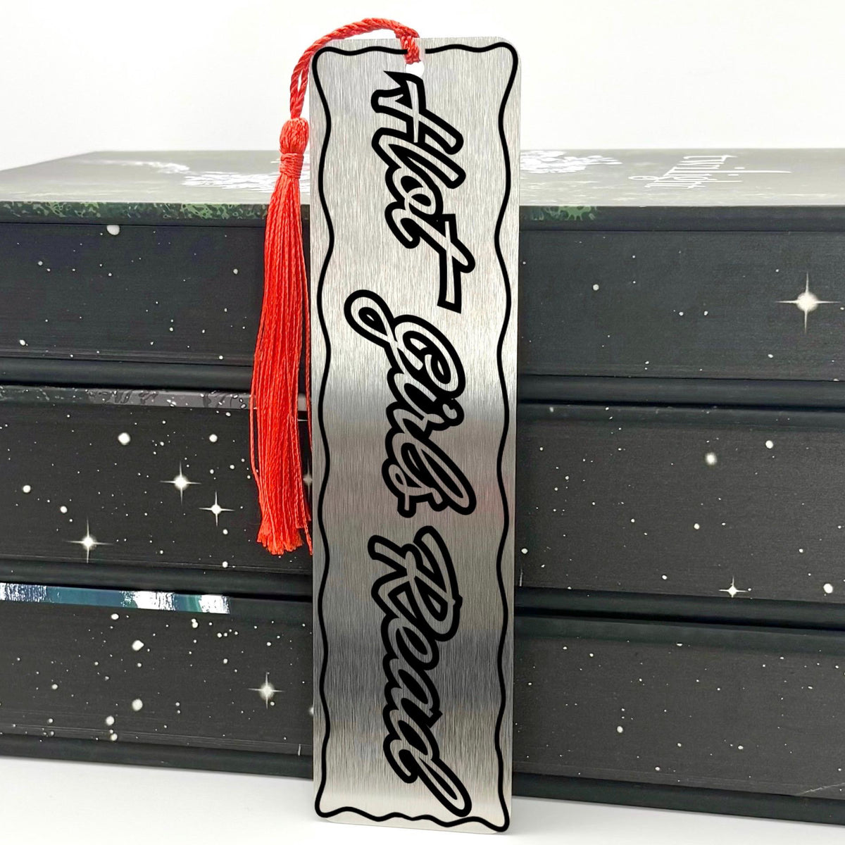 Hot Girls Read Metal Engraved Bookmark displayed with red tassel on stacked black books.