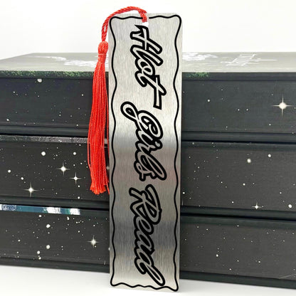 Hot Girls Read Metal Engraved Bookmark displayed with red tassel on stacked black books.