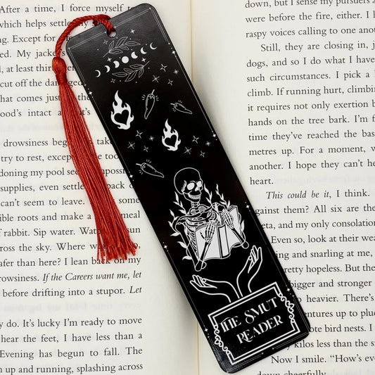 A black The Smut Reader Metal Bookmark on and open book with a red tassel