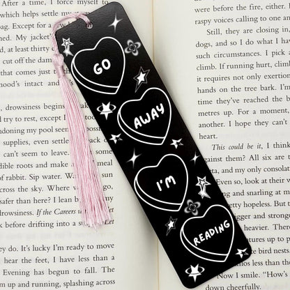     Go Away I’m Reading Metal Bookmark in black with engraved heart and celestial design displayed on an open book