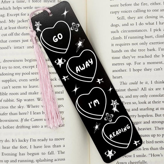     Go Away I’m Reading Metal Bookmark in black with engraved heart and celestial design displayed on an open book