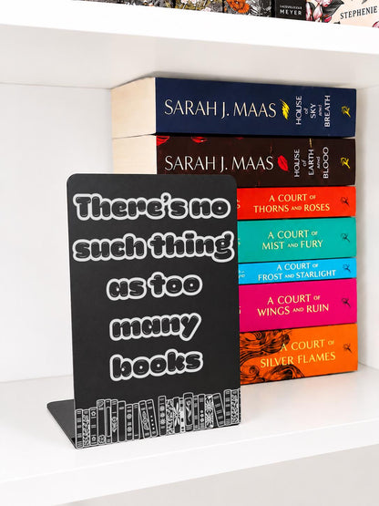     There Is No Such Thing As Too Many Books Metal Bookshelf Sign Bookend displayed with a colourful stack of fantasy books on a white bookshelf.