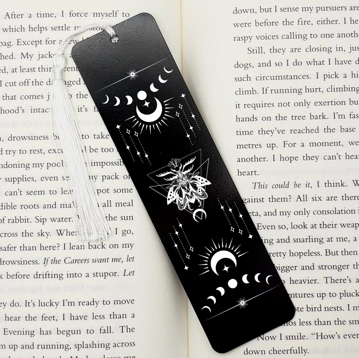 A black Celestial Moon and Stars Metal Bookmark on and open book with a white tassel
