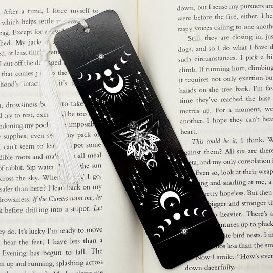 A black Celestial Moon and Stars Metal Bookmark on and open book with a white tassel