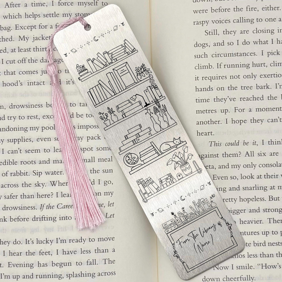 A brushed silver Personalised Name Library Shelf Metal Bookmark on and open book with a pink tassel