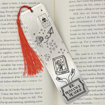 A brushed silver The Romance Reader Metal Bookmark on and open book with a red tassel